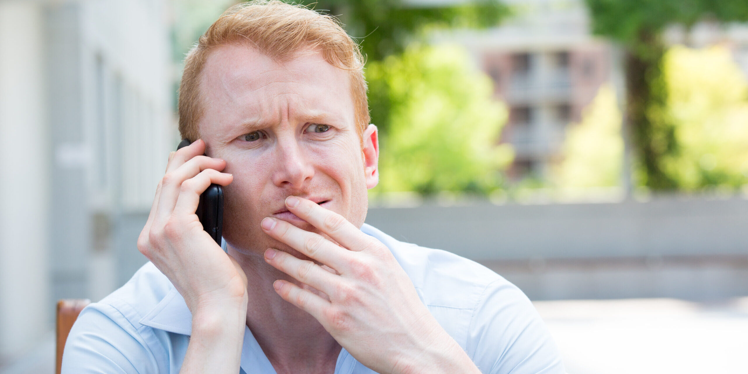 Closeup portrait young man perplexed baffled befuddled bewildered by someone talking on his mobile phone isolated outdoors background What is considered a dental emergency?