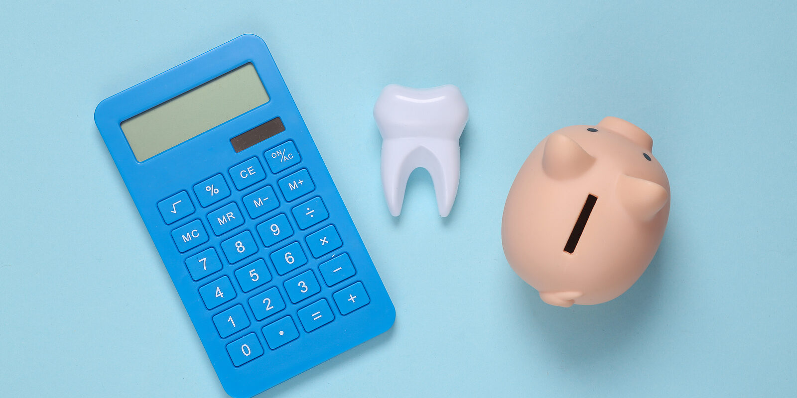 dental implants cost Dental treatment costs. Piggy bank, calculator and tooth on blue background. Top view